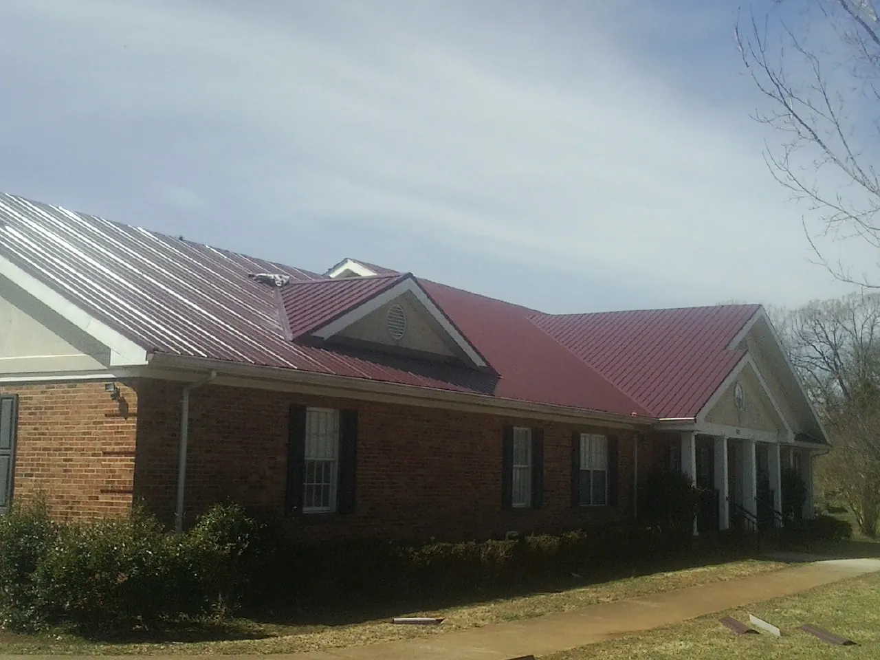 Red metal roof with gabled entries on a long brick building, from a Hail Damage Roof Repair job in Aspers