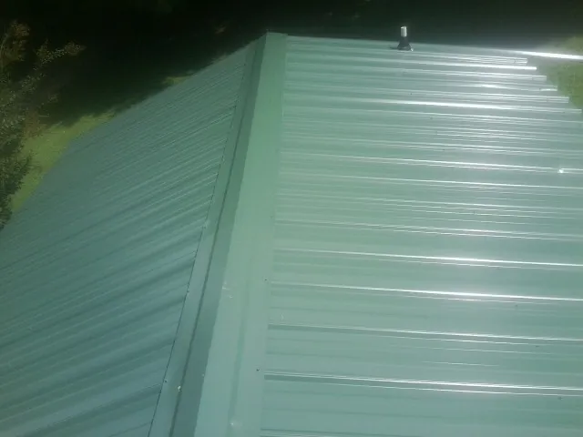 New green metal panels meeting at the ridge of a roof — Flat Roof Repair work by our crew in Aspers