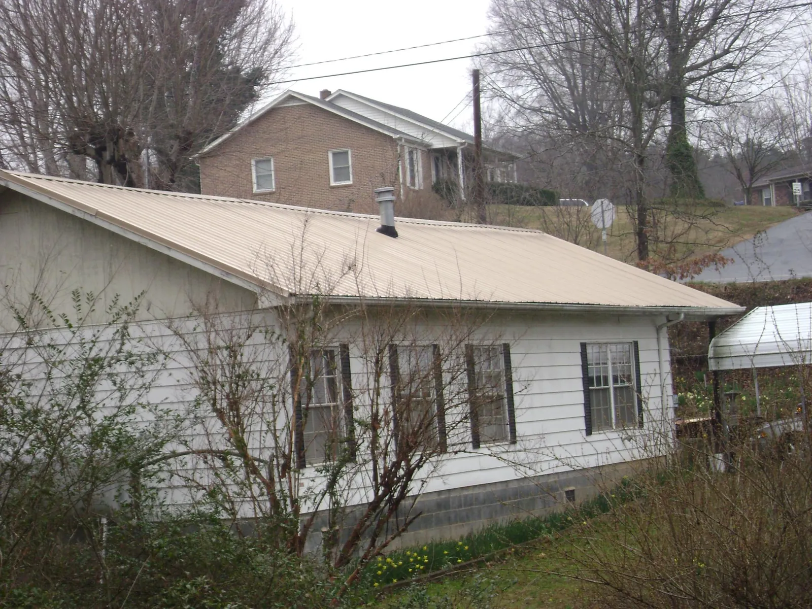 Tan metal roof on a white sided house set into a hillside — Commercial Roofing by Roofing Brothers in Aspers